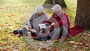 Senior Caucasian married couple read together on the ground in the park full shot selective focus