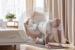 Senior caucasian men practices yoga asana chakravakasana, bird pose at home