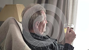 Senior caucasian old man swinging in rocking chair and drinking tea. Side view of positive senior male retiree waving