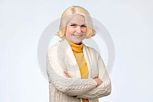 Senior caucasian woman with blonde hair in white and yellow sweater smiling