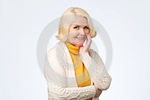 Senior caucasian woman with blonde hair in white and yellow sweater smiling