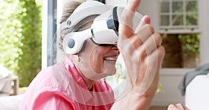 Senior Caucasian woman is engaged with a virtual reality headset, smiling broadly