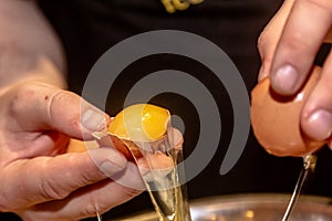 senior caucasian woman hands breakes white chicken egg above white bowl at domestic kitchen