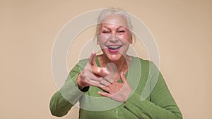 Senior caucasian woman laughing at your funny joke, pointing finger to the camera.
