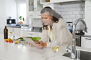 Senior caucasian woman in modern kitchen, using tablet computer