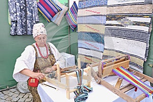 Senior Caucasian woman in traditional Russian dress weaving colorful striped rug on hand loom