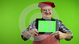 Senior chef in red apron showing tablet with blank advertising display.