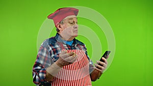 Senior chef in red apron talking with phone webcam about things at his life.