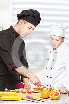 Senior chef teaches young chef to decorate fruit