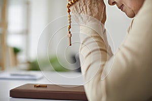 Senior Christian woman praying to God and holding rosary beads over the Holy Bible