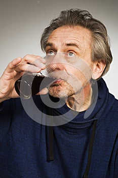 Senior citizen drinking a glass of red wine in studio