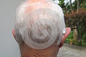 Senior citizen man wearing modern digital high technology hearing aid in ear back view