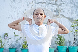 Senior Citizen or an Old Indian Man Performing Yoga Early Morning, in his Terrace in white Tshirt and Pants. Stay Home Stay Safe a