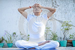 Senior Citizen or an Old Indian Man Performing Yoga Early Morning, in his Terrace in white Tshirt and Pants. Stay Home Stay Safe a