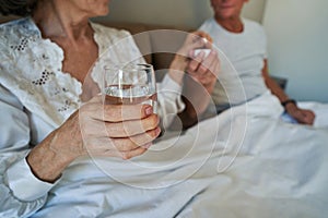 Senior citizen talking pill while holding glass of water