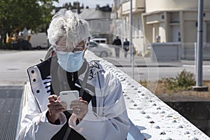 A senior citizen wearing a mask writes or reads an SMS