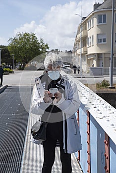 A senior citizen wearing a mask writes or reads an SMS