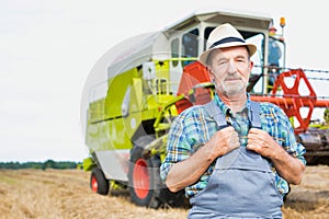 Senior confident farmer standing against harvester in field