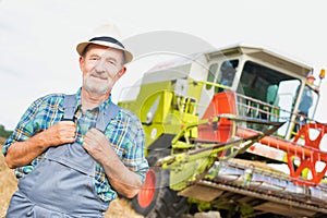 Senior confident farmer standing against harvester in field