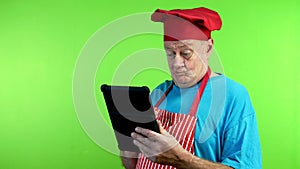 Senior cook in apron reads recipe on tablet, not understand anything.