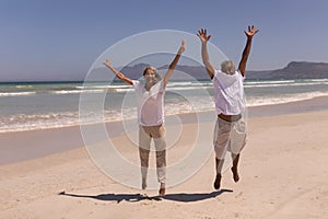 Senior couple with arms up jumping on beach