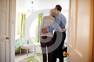 Senior couple arrive embracing in a hotel room, back view