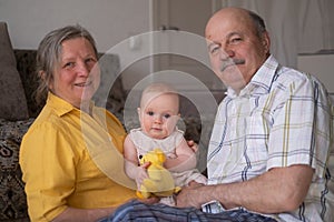 Senior couple with baby granddaughter posing sitting at home