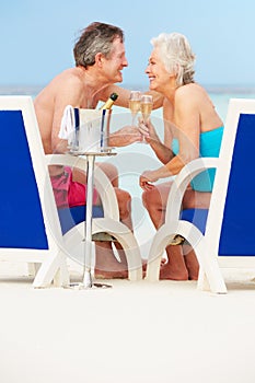 Senior Couple On Beach Relaxing In Chairs Drinking Champagne