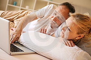 Senior couple in bed using laptop.