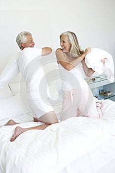 Senior Couple In Bedroom Having Pillow Fight