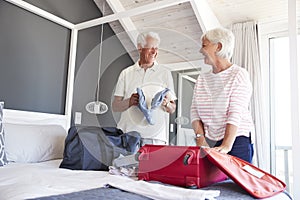 Senior Couple In Bedroom Packing Suitcase For Vacation photo