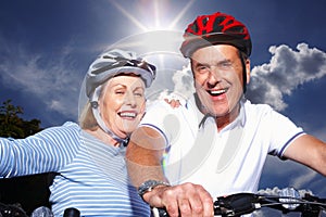 Senior couple with bicycles and protective helmet on a sunny day. Closeup portrait of a cheerful senior couple with