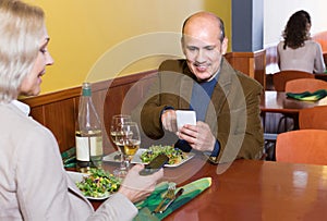 Senior couple busy with phones on date in cafe
