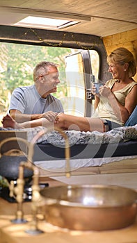 Senior Couple Camping In Countryside Relaxing Drinking Coffee Inside RV