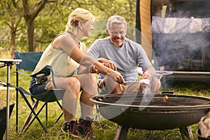 Senior Couple Camping In Countryside With RV Toasting Marshmallows Outdoors On Fire