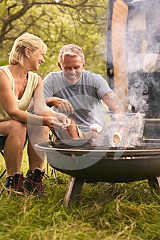 Senior Couple Camping In Countryside With RV Toasting Marshmallows Outdoors On Fire