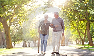 Senior couple, cane and walking outdoor at a park with a love, care and support for health and wellness. A elderly man