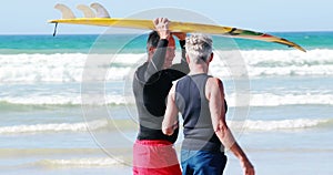 Senior couple carrying surfboard over head while walking on beach