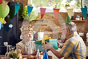 Senior couple celebrating together, elderly birthday woman recieving birthday gift present from her husband sitting at dinner