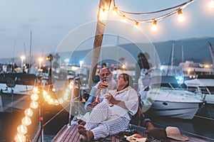 Senior couple cheering with champagne and eating watermelon on boat - Old people having fun together drinking and laughing -