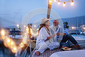 Senior couple cheering with champagne on a sailboat during wedding anniversary vacation - Old people having fun together drinking