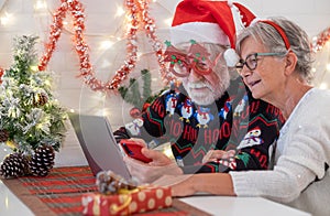 Senior couple in Christmas sweeter and santa hat while using laptop computer and mobile phone. Elderly happy couple celebrate