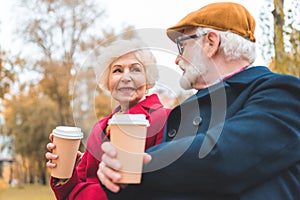 senior couple with coffee to go sitting on bench