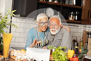 Senior couple cooking dinner together and searching recipes on t