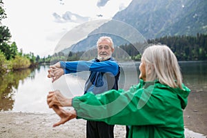 Senior couple doing outdoor yoga by the lake in the mountains.