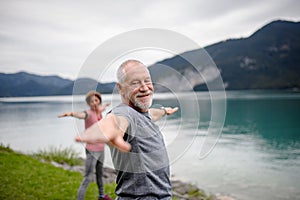 Senior couple doing outdoor yoga, tai chi, pilates by the lake in the autumn. Elderly husband and wife spending active