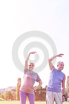 Senior couple doing stretching exercise in park against sky