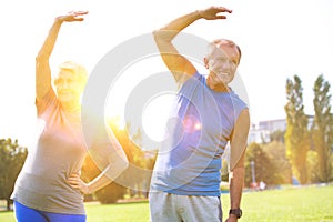 Senior couple doing stretching exercise in park against sky