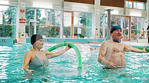 Senior couple doing stretching exercises using swim noodles in the swimming pool