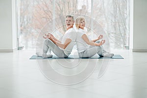 Senior couple doing yoga in the class and looking at camera and smiling. Lifestyle, health and sport concept